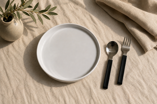 White plate with black cutlery on a beige surface with a plant in the background